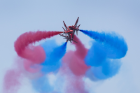 Royal Air Force Red Arrows performing maneuvers in the sky with red and blue smoke coming out the rear of the planes